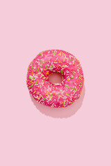 Donut in pink glaze with colorful sprinkles on a pink background
