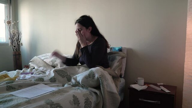 Student girl with flu sneezes sitting on a double bed