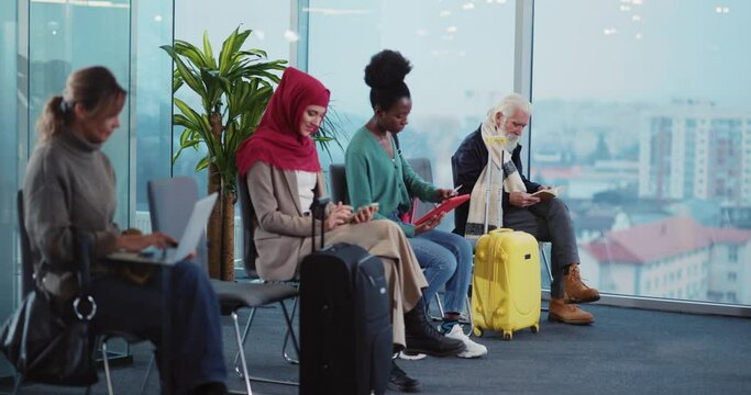 Multi-cultural stylish people sitting in waiting area before flight using mulptiple computer devices. Departure lounge. Airport terminal.