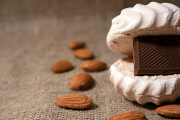 White zephyr with tile of dark chocolate inside and scattered peeled almonds lying on a sack cloth