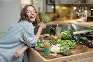 Pretty young woman holding healthy green broccoli on the kitchen. Cooking diet salad with vegetable...