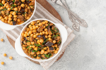 Cooked chickpeas with eggplant, parsley, olive oil, garlic, and spices in a white bowl on a grey background top view. Vegetarian food, Middle Eastern cuisine. Copy space for text