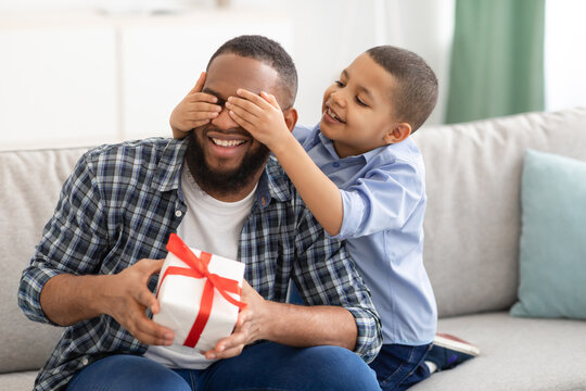 Little Son Congratulating Black Father Giving Wrapped Gift Indoors