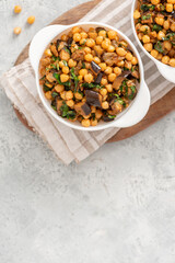 Cooked chickpeas with eggplant, parsley, olive oil, garlic, and spices in a white bowl on a grey background top view. Vegetarian food, Middle Eastern cuisine. Copy space for text
