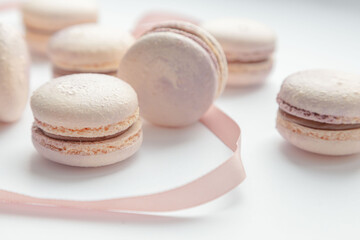 Lots of delicate French macaroons lie on a white background with a pink ribbon. Vintage. Advertising. Desser. Postcard. Place for an inscription. View from above. Dessert with tea. Confectioner.