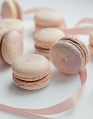 Lots of delicate French macaroons lie on a white background with a pink ribbon. Vintage. Advertising. Desser. Postcard. Place for an inscription. View from above. Dessert with tea. Confectioner.