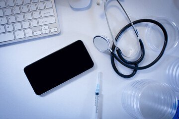 Desk in doctors surgery with smartphone computer keyboard syringe and stethoscope