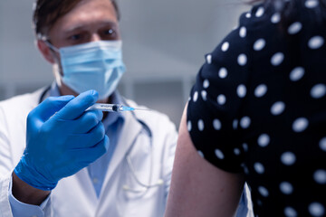 Caucasian male doctor wearing face mask and gloves giving vaccine to patient