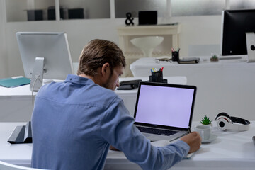 Caucasian businessman sitting at desk using laptop in an empty office