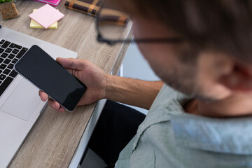 Fototapeta na wymiar Over shoulder view of caucasian man sitting at desk making video call using smartphone