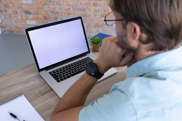 Over shoulder view of caucasian man sitting at desk making video call using laptop