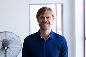 Portrait of smiling caucasian man standing in front of window in white room