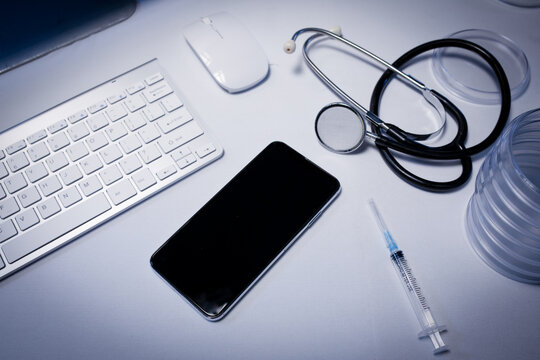 Desk in doctors surgery with smartphone computer keyboard syringe and stethoscope - Powered by Adobe