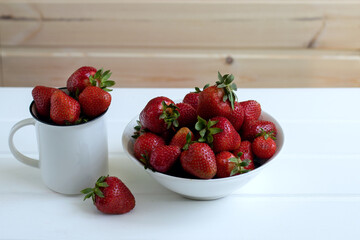 red juicy ripe strawberries in a white dish on a white wooden background, berries, vitamins, space for text