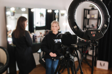 Woman make makeup for attractive blond hair woman in studio. Selective focus of digital camera with makeup artist applying cosmetics for beautiful model