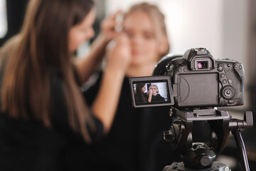 Naklejka premium Woman make makeup for attractive blond hair woman in studio. Selective focus of digital camera with makeup artist applying cosmetics for beautiful model