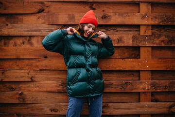 Fashionable girl in great mood posing on wooden background. Woman in baggy jeans, emerald coat and...