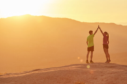 Side view of friendly sportsman and sportswoman giving high five to each other while standing on hill in highlands at sunset