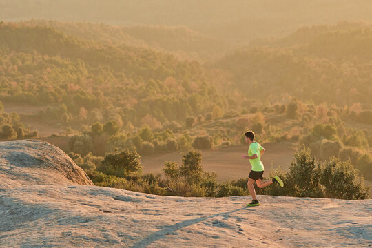 Side view of slim male runner running on rocks in mountains at sunset in evening during active training