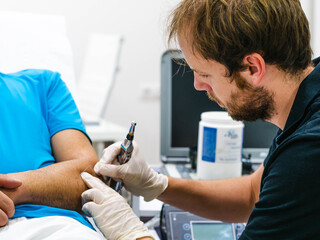 Side view of male medical practitioner in protective goggles using laser probe to cure arm of crop patient during work in physiotherapy clinic