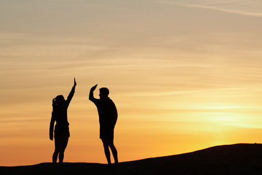 Side view of friendly sportsman and sportswoman giving high five to each other while standing on hill in highlands at sunset