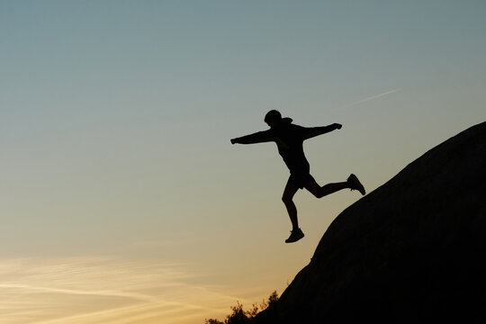 Side view of silhouette of anonymous male athlete jumping from hill during dynamic training in highlands at sunset