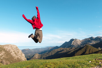 Back view of excited hiker jumping above ground in highlands and enjoying summer vacation in El Mazuco