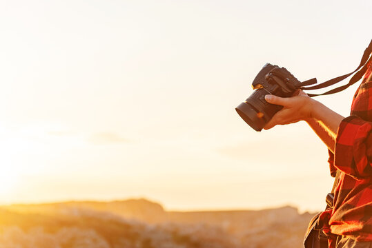 Crop of side view of unrecognizable female traveler with professional photo camera standing on hill in mountainous area