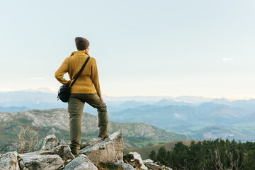 Back view of unrecognizable explorer standing on rough rock and enjoying scenery of highlands during vacation