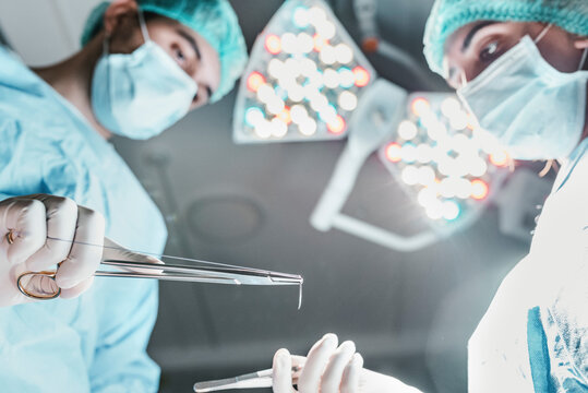 From below side view of focused professional surgeon and nurse with medical scissors working together in operating room in modern hospital