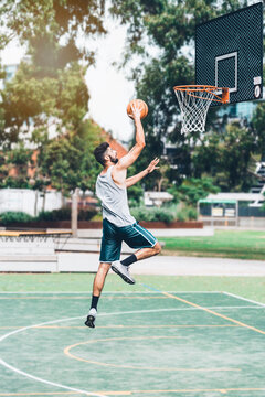 Full Body Side View Of Determined Young Male Basketball Player In Sportswear Leaping And Shooting Ball Near Hoop While Training Alone On Street Playground