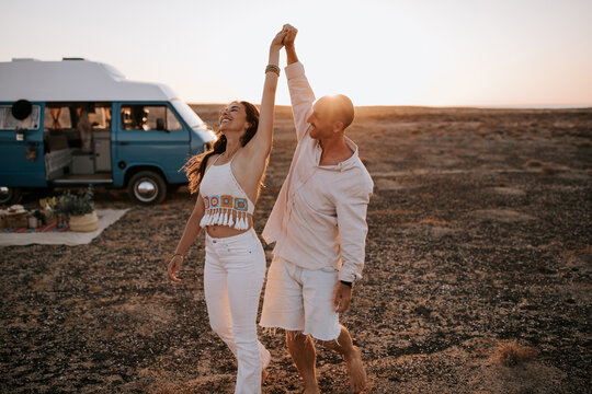 Side view of positive traveling couple in white clothes hugging and standing in savanna on background of sundown sky during summer vacation