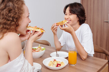 Cheerful hungry young women having delicious pizza, salad and apple slices for dinner