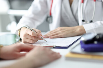 Doctor advising patient and writing in documents closeup