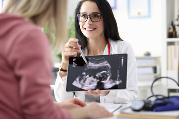 Gynecologist showing patient ultrasound of fetus on tablet