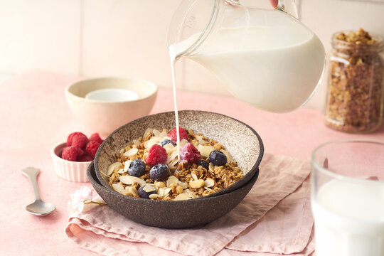 Hand with a jug pouring milk to granola with berries