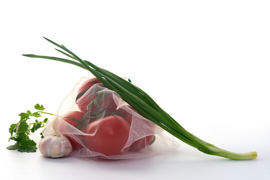 Still life with tomatoes in net mesh bag back lit on white background