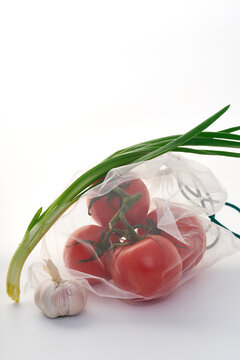 Still life with tomatoes in net mesh bag back lit on white background