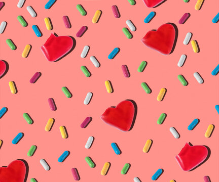 Top view of pattern of red heart shaped and colorful small jelly candies on pink background