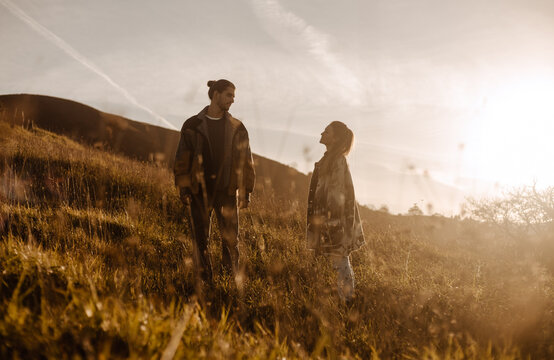 Loving couple in stylish retro clothes standing in field at sundown looking at each other