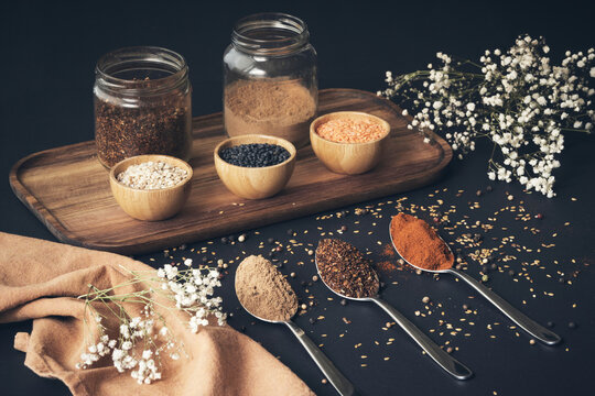 Top view of assorted grains in jars and aromatic spices in spoons arranged on wooden tray on black table - Powered by Adobe
