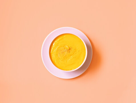 Top view of bowl of appetizing pumpkin cream soup placed on pink background in studio