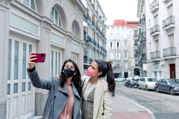 Two women taking a selfie in the street with their face masks on.