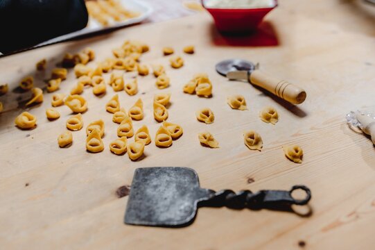 From above raw traditional tortellini scattered on wooden table in kitchen with wheel cutter and flatten dough