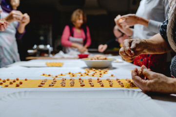Crop unrecognizable housewives preparing Italian tortellini from dough and raw meat on table in kitchen