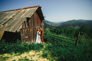 Wedding couple in the mountains. The groom and bride are hugging near the rustic house. A beautiful view of the mountains behind the couple