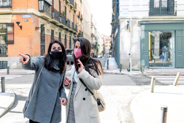 Two women pointing out where to go in the street with their face masks on.