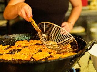 Crop unrecognizable chef with metal ladle frying pieces of dough in pan with hot oil while working in professional kitchen