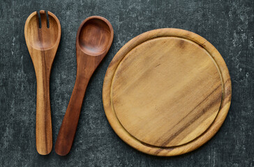 Wooden salad spoons lie next to a round cutting board, kitchen utensils, vintage style. Top view