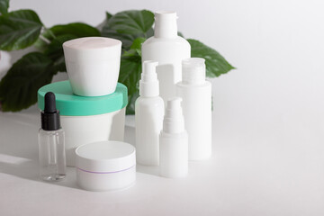 Fototapeta na wymiar Cosmetic bottles stand next to green leaves on a white background. Organic cosmetics concept